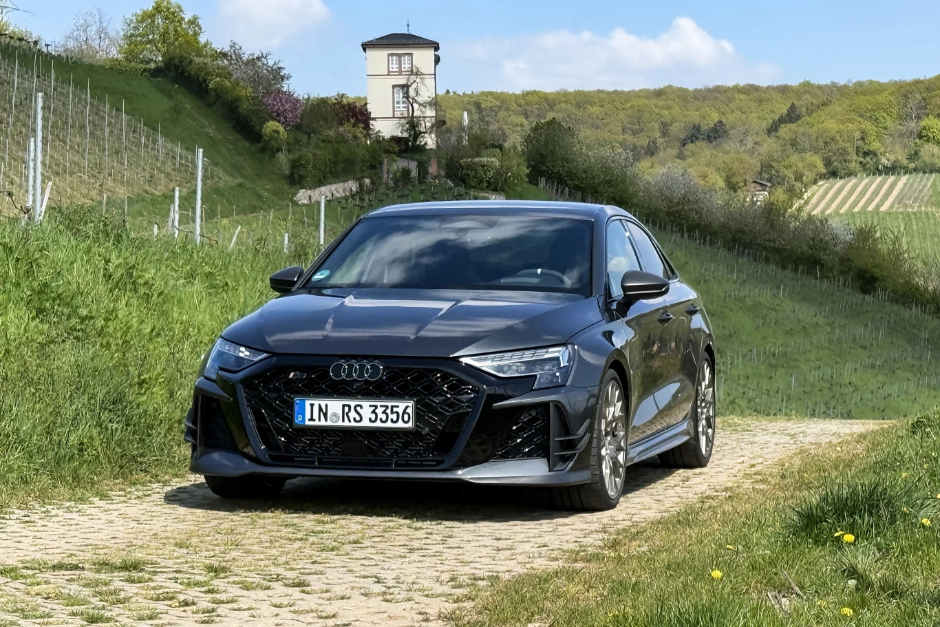 Audi RS3 Competition Limited w pełnej krasie. Czy to ostatnie RS3 w Europie? czarne sportowe audi rs3 zaparkowane na kamiennej ścieżce między zielonymi wzgórzami, w tle winnica i wieża na wzgórzu