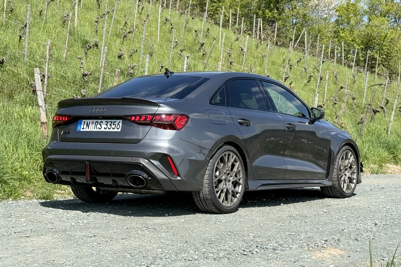 Competition Limited to w dużej mierze pakiet wizualnych modyfikacji bazowego RS3. ciemnoszary sportowy sedan Audi RS, z dużymi felgami aluminiowymi, podwójnymi końcówkami układu wydechowego i charakterystycznymi tylnymi światłami LED, zaparkowany na szutrowej drodze wśród zielonych krzewów winnicy