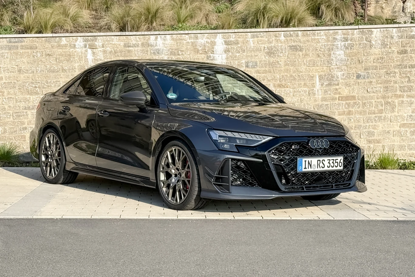 Competition Limited to RS3 "kompletne". Ponadto świetna lokata kapitału. czarne Audi RS3 z agresywnie stylizowanym przodem, dużymi aluminiowymi felgami i czerwonymi zaciskami hamulcowymi zaparkowane na jasnej kostce brukowej na tle kamiennego muru