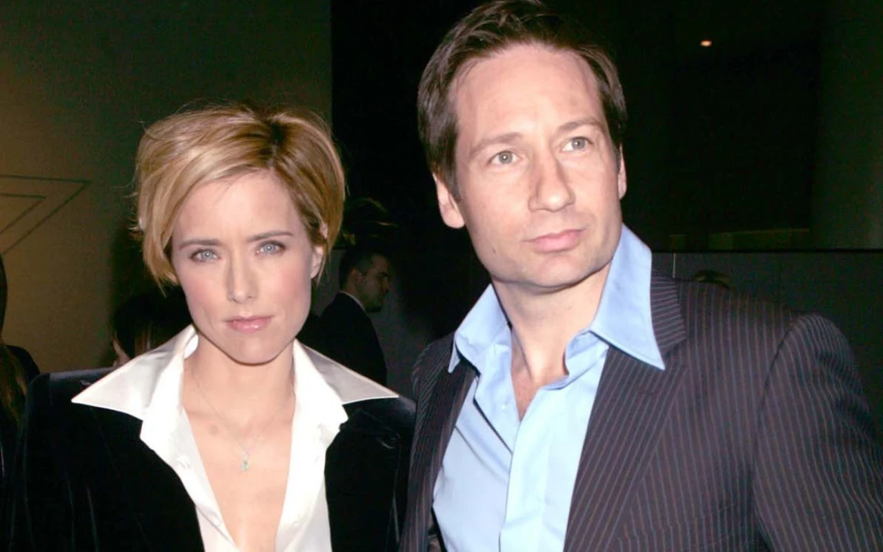 Kobieta i mężczyzna stoją obok siebie w eleganckich, wieczorowych ubraniach, patrząc w kierunku aparatu; oboje mają poważne miny, a tło jest neutralne i przyciemnione.