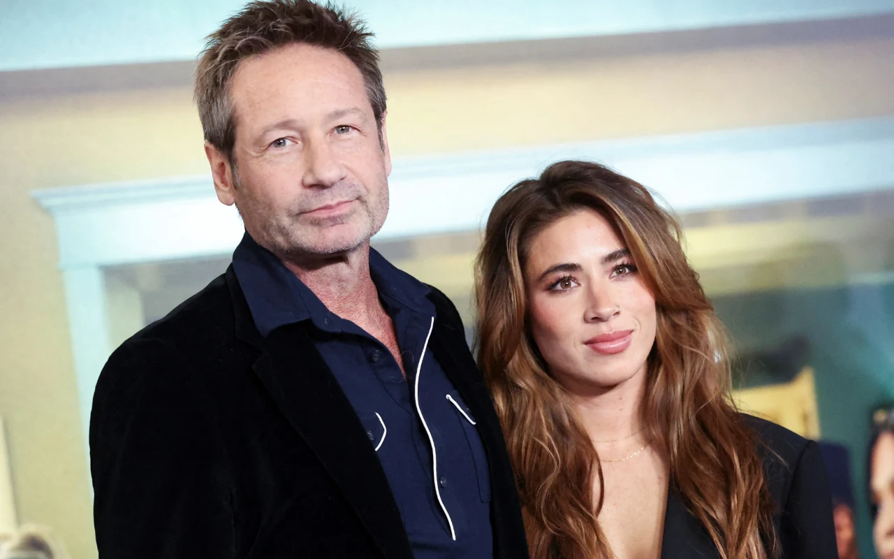 Mężczyzna w ciemnej marynarce i koszuli oraz młoda kobieta o długich, brązowych włosach stoją razem, patrząc w stronę obiektywu; oboje wyglądają elegancko, co sugeruje udział w ważnym wydarzeniu.