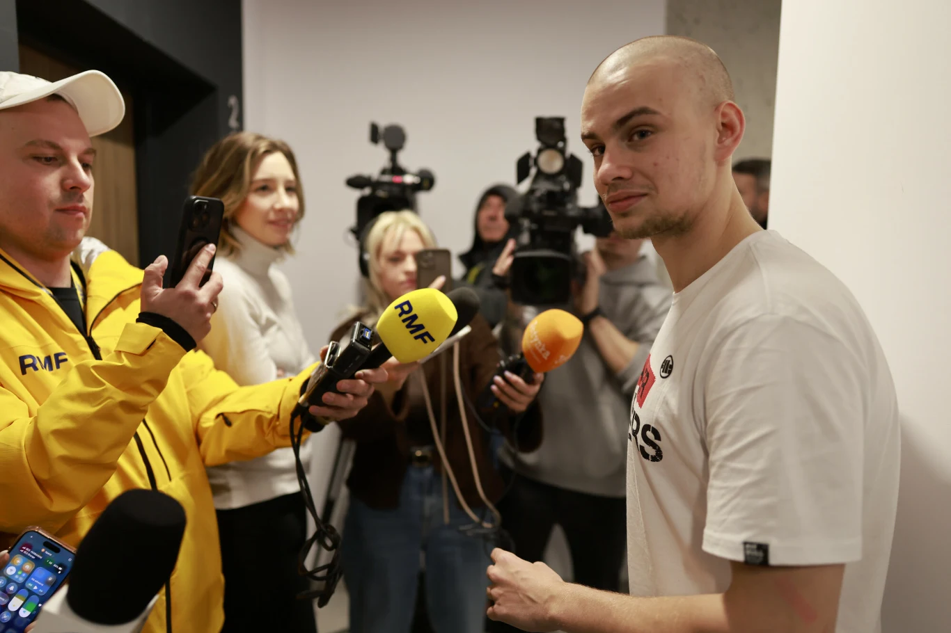 mężczyzna udzielający wywiadu grupie reporterów wyposażonych w mikrofony i kamery, w centrum uwagi znajduje się rozmowa, a na mikrofonach widoczne są logotypy stacji radiowych
