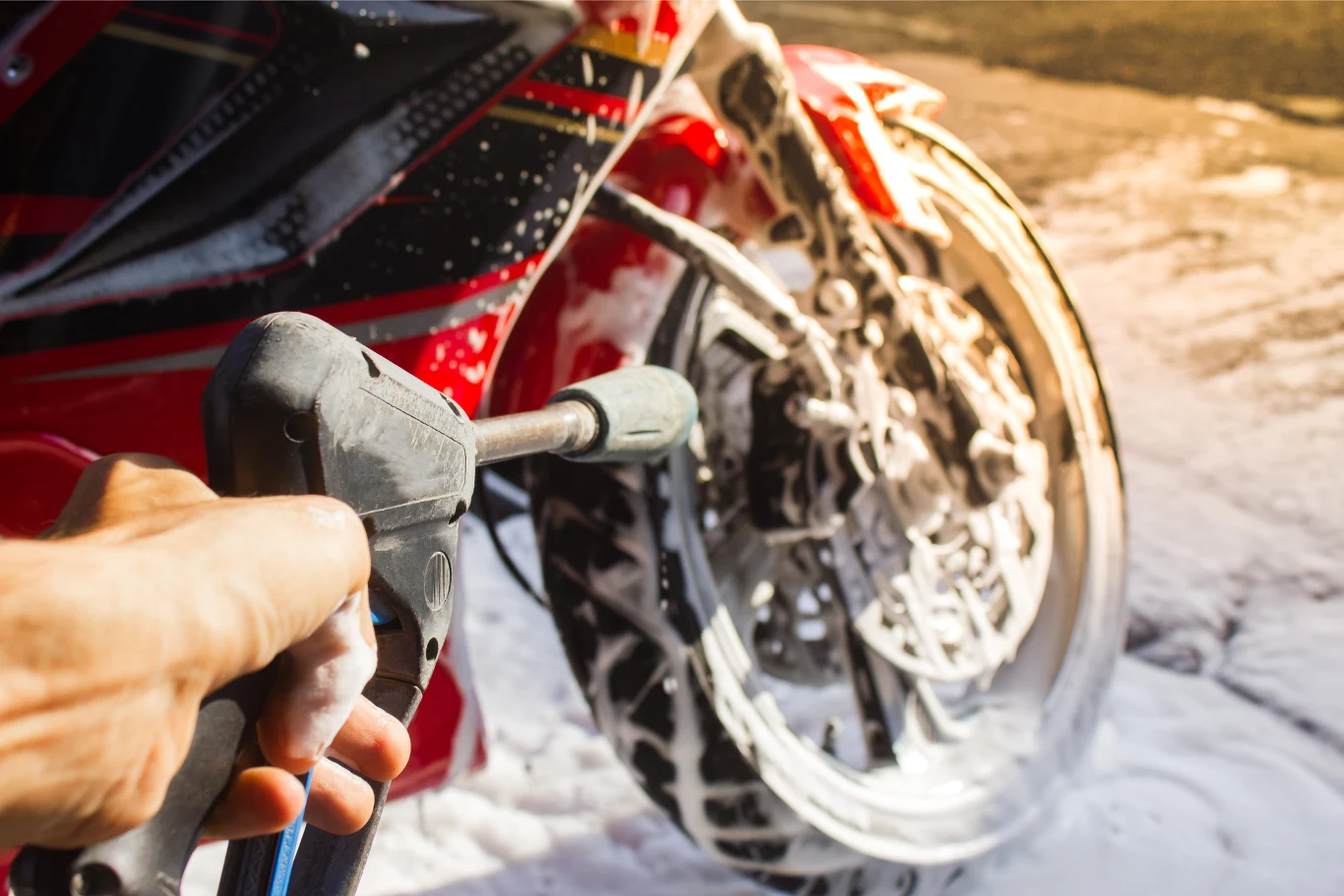 mycie motocykla pianą aktywną za pomocą myjki ciśnieniowej, zbliżenie na przednie koło i rękę trzymającą lancę