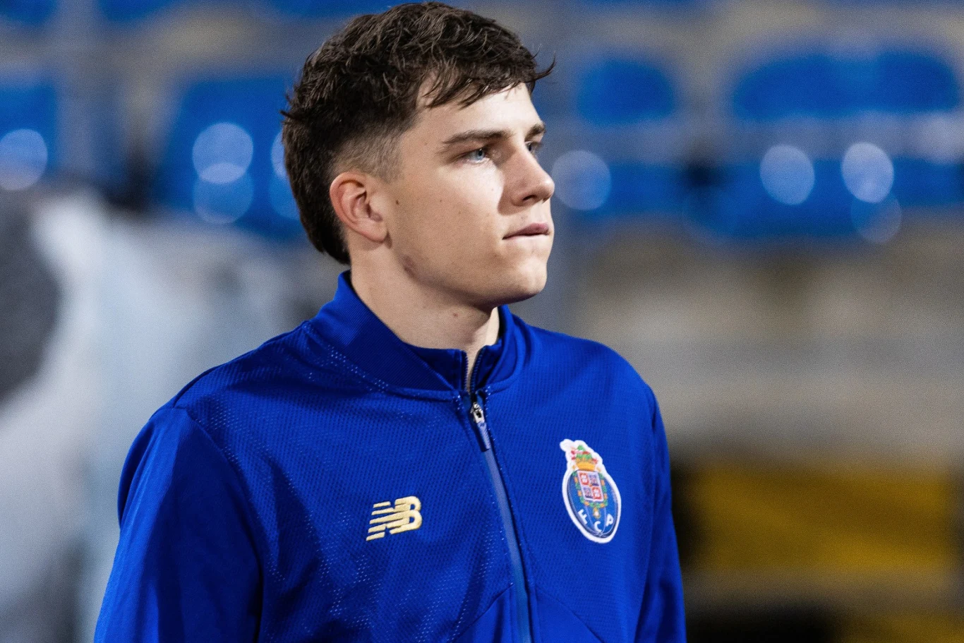 Oskar Pietuszewski młody mężczyzna w sportowej kurtce w barwach klubu FC Porto stoi na tle pustych, niebieskich trybun i patrzy w bok