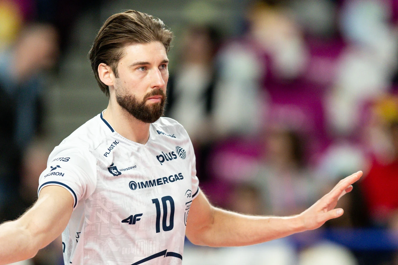 Bartosz Bednorz siatkarz w białej koszulce z numerem 10 i sponsorami na piersi, z rozłożonymi ramionami podczas gry, skupiony wyraz twarzy i dynamiczna postawa