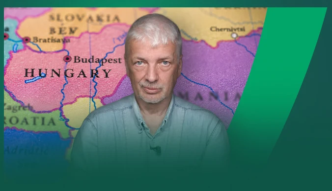 mężczyzna o siwych włosach i jasnej koszuli na tle kolorowej mapy Europy Środkowej z widocznymi nazwami krajów, takich jak Węgry, Słowacja, Chorwacja oraz miasta Budapeszt