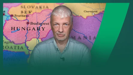 mężczyzna o siwych włosach i jasnej koszuli na tle kolorowej mapy Europy Środkowej z widocznymi nazwami krajów, takich jak Węgry, Słowacja, Chorwacja oraz miasta Budapeszt