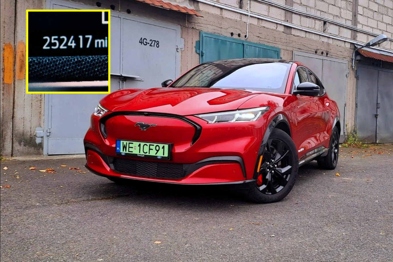 Przejechał autem elektrycznym prawie pół miliona kilometrów. / Zdj. ilustracyjne Czerwony Ford Mustang Mach-E na tle szarej zabudowy, licznik 252417 mil, polska zielona tablica rejestracyjna