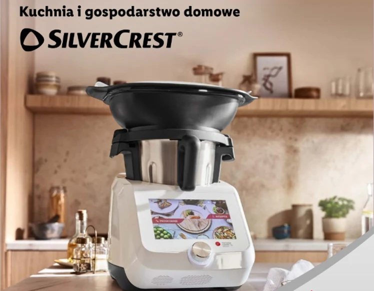 Wielofunkcyjne urządzenie kuchenne SILVERCREST z dużym ekranem dotykowym i zamontowaną czarną misą, ustawione na blacie w nowoczesnej kuchni z drewnianymi półkami i akcesoriami w tle.