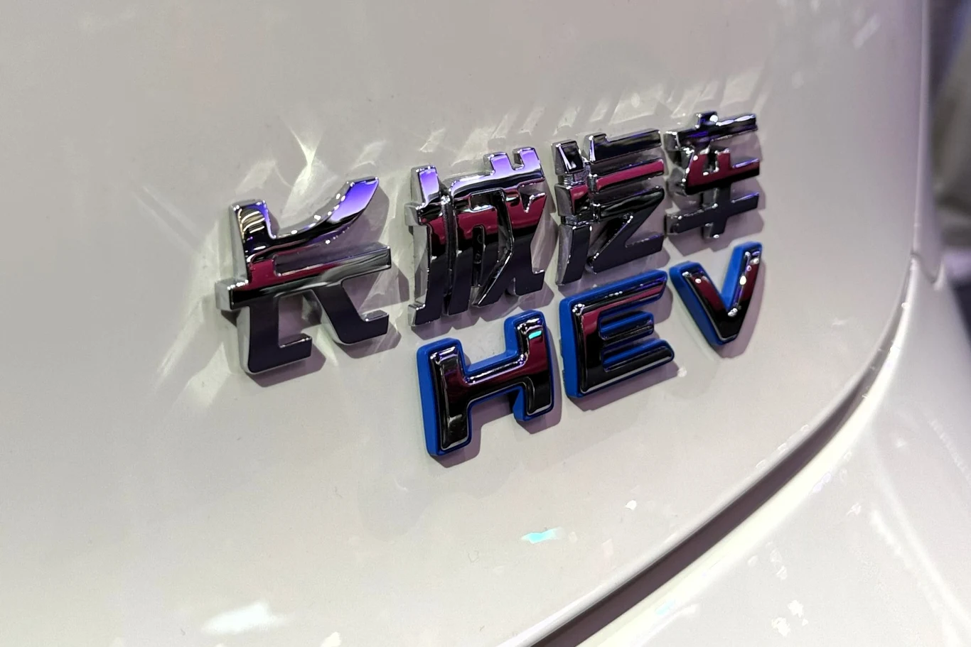 Układ hybrydowy ma generować 223 KM. metaliczne logo z chińskimi znakami oraz literami HEV na białym nadwoziu samochodu, podkreślające hybrydową technologię pojazdu