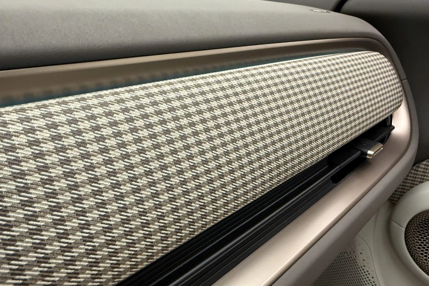 Materiały są przyjemne w dotyku, np. ten kraciasty materiał. panel deski rozdzielczej samochodu pokryty materiałem w pepitkę, z wbudowanym nawiewem i częścią głośnika widoczną po prawej stronie
