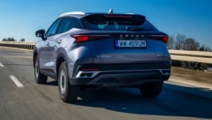 srebrny SUV Omoda C5 z polską rejestracją porusza się po pustej, dwupasmowej autostradzie w słoneczny dzień, na tle niebieskiego nieba i niskiej roślinności przy drodze