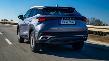srebrny SUV Omoda C5 z polską rejestracją porusza się po pustej, dwupasmowej autostradzie w słoneczny dzień, na tle niebieskiego nieba i niskiej roślinności przy drodze