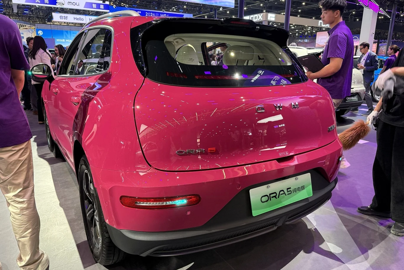GWM Ora 5 będzie pierwszym modelem chińskiego koncernu oferowanym w Polsce. różowy samochód elektryczny ORA 03 wyeksponowany na targach motoryzacyjnych, wokół auta stoją ludzie w fioletowych koszulkach