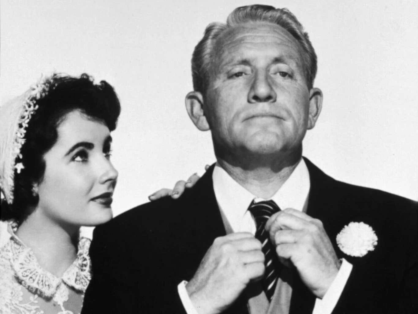 Elizabeth Taylor i Spencer Tracy w filmie "Ojciec narzeczonej" Elegancko ubrana młoda kobieta w welonie patrzy z podziwem na starszego mężczyznę w garniturze, który poprawia krawat, z przypiętym do klapy kwiatem.