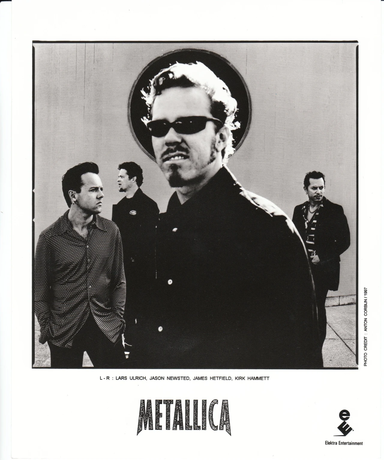 Metallica przy okazji premiery płyty "Reload" w 1997 r. Czterech mężczyzn ubranych na czarno stoi na tle jasnej ściany, a jeden z nich, znajdujący się na pierwszym planie, nosi okulary przeciwsłoneczne i dominuje w kadrze; reszta grupy patrzy w różnych kierunkach.