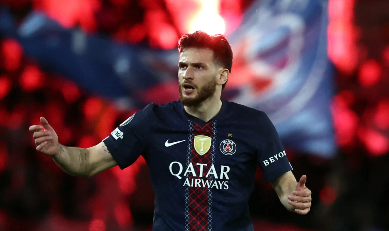 piłkarz Paris Saint-Germain w granatowym stroju z wyraźnie widocznym herbem i napisem Qatar Airways gestykuluje na boisku podczas meczu, w tle rozmyta flaga klubowa na stadionie oświetlonym czerwonym światłem