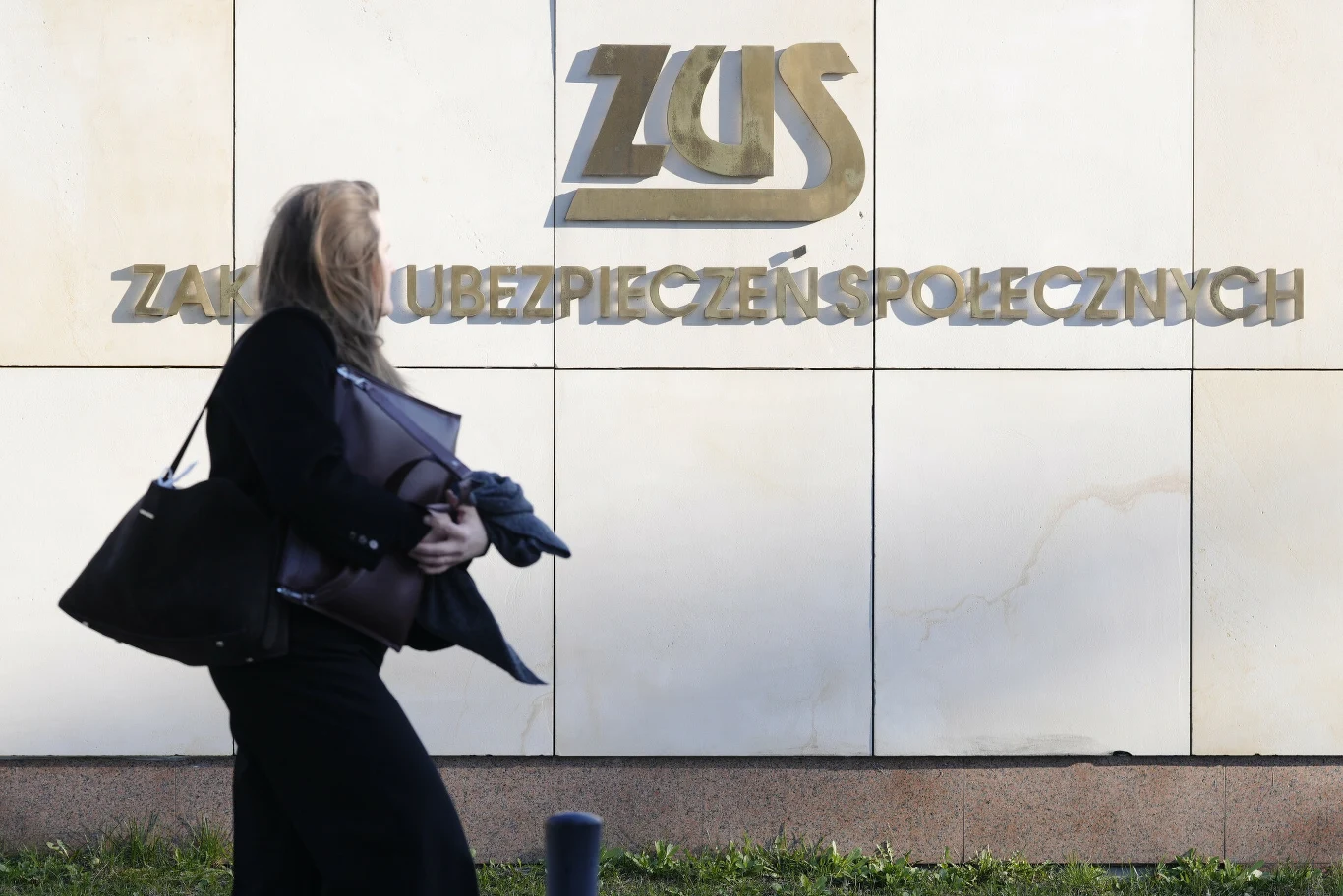 ZUS opublikował szczegółowe dane ws. L4 za ubiegły rok Kobieta idzie obok budynku ZUS z dużym napisem Zakład Ubezpieczeń Społecznych na ścianie.