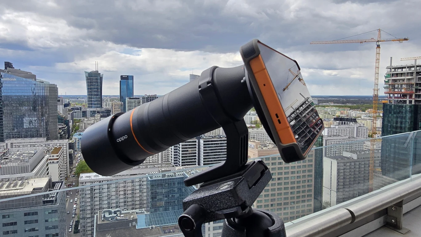 Smartfon z telekonwerterem Hasselblad. telefon komórkowy zamontowany na statywie z dużym teleobiektywem skierowanym w stronę panoramy miejskiej z nowoczesnymi wieżowcami i żurawiem budowlanym w tle