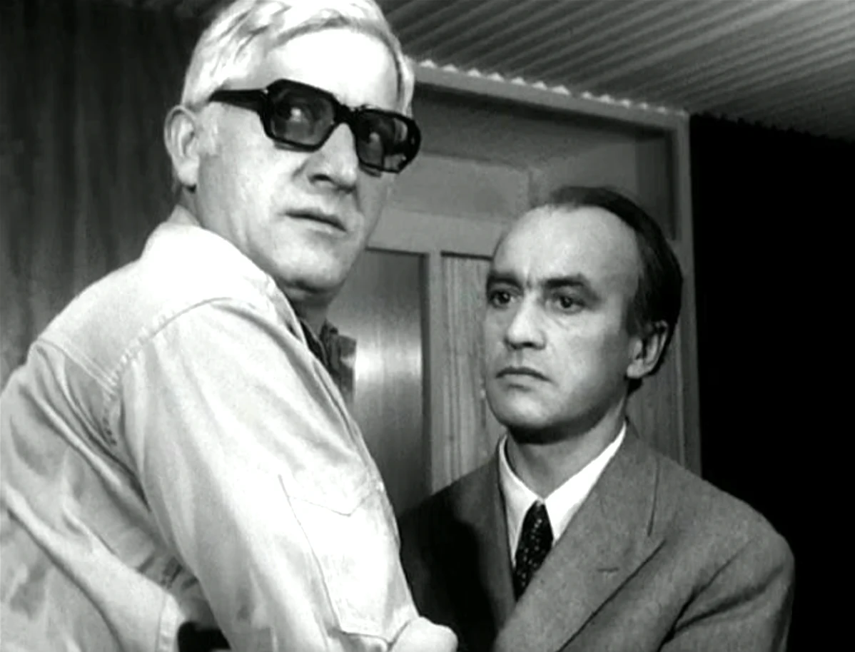 Kadr z filmu "Hydrozagadka" (1971) Dwóch mężczyzn stoi blisko siebie w pomieszczeniu. Patrzą poważnie przed siebie.