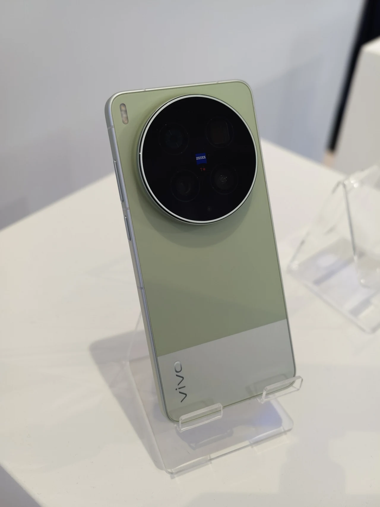 vivo X300 Ultra to świetny smartfon w wielu aspektach Nowoczesny smartfon Vivo w jasnozielonej obudowie z dużym, okrągłym, czarnym modułem aparatu fotograficznego umieszczonym na górze tylnej części obudowy, prezentowany na przezroczystej podstawce ekspozycyjnej.