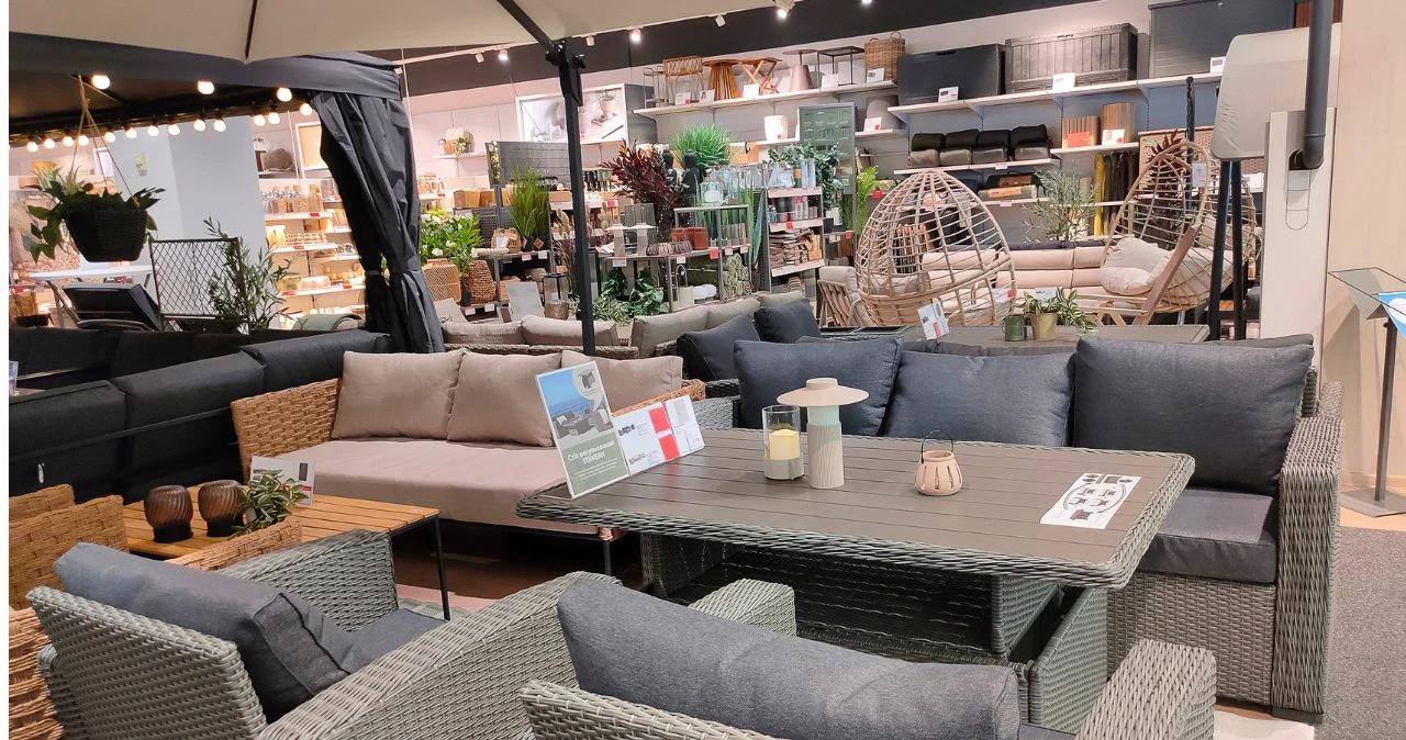 Meble ogrodowe JYSK przecenione nawet o 60% – co warto kupić? Ekspozycja mebli ogrodowych JYSK: szary stół, fotele, kanapa, świeczniki, fotele wiszące i rośliny doniczkowe