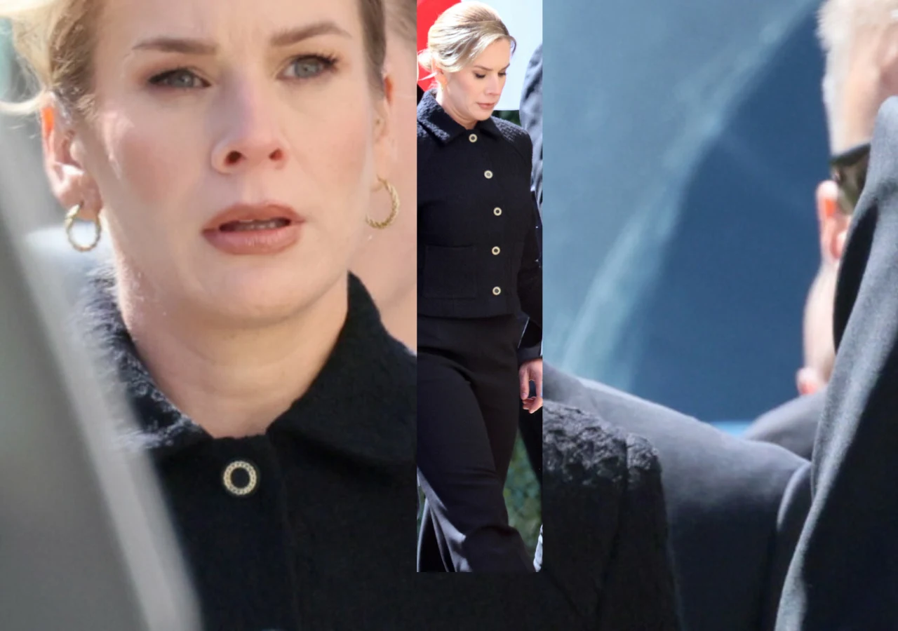 Kobieta w czarnym eleganckim płaszczu z dużymi guzikami i złotymi kolczykami w kształcie kółek, o jasnych włosach spiętych do tyłu, z poważnym wyrazem twarzy; w tle rozmyte postacie i fragmenty ubioru innych osób.