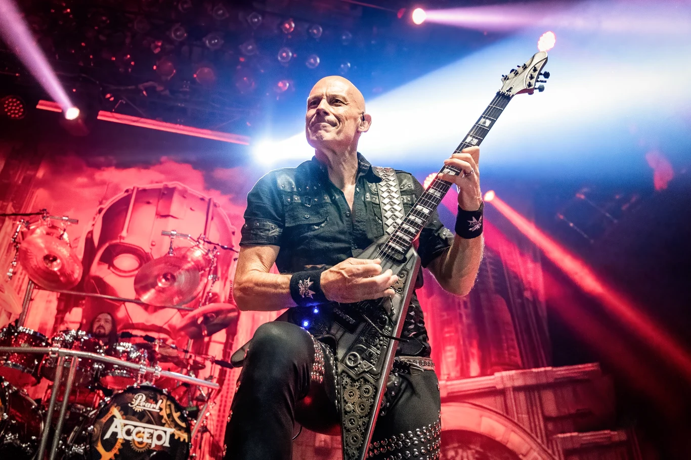 Wolf Hoffmann stoi na czele grupy Accept Wolf Hoffmann, łysy gitarzysta Accept w skórzanej kamizelce, gra na scenie z bębnami z logo zespołu w tle