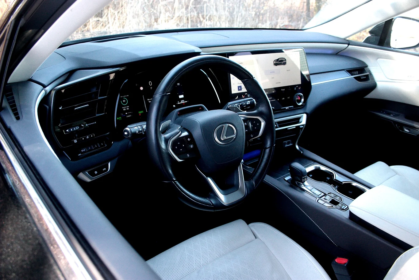 wnętrze luksusowego samochodu Lexus z elegancką, czarną kierownicą z logo marki, cyfrowym kokpitem oraz dużym ekranem multimedialnym na konsoli środkowej, a także jasnymi, skórzanymi fotelami