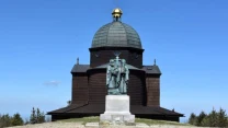 drewniana kaplica z dużą kopułą i złotym zwieńczeniem pośrodku, przed którą stoi okazały pomnik dwóch postaci na kamiennym cokole
