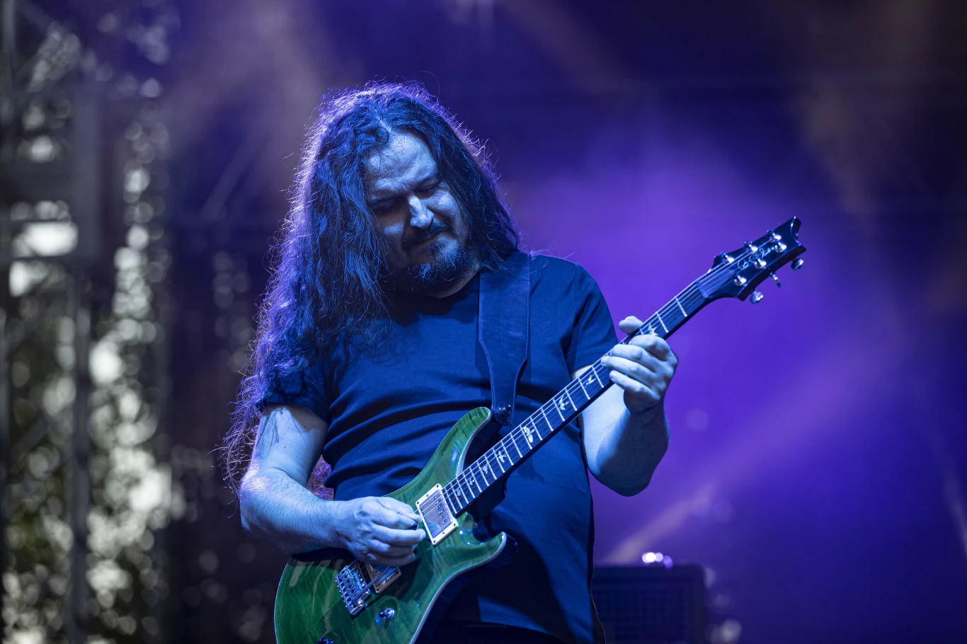 Maciej Meller w składzie Riverside Maciej Meller gra na gitarze elektrycznej podczas koncertu Riverside, oświetlony fioletowym światłem.