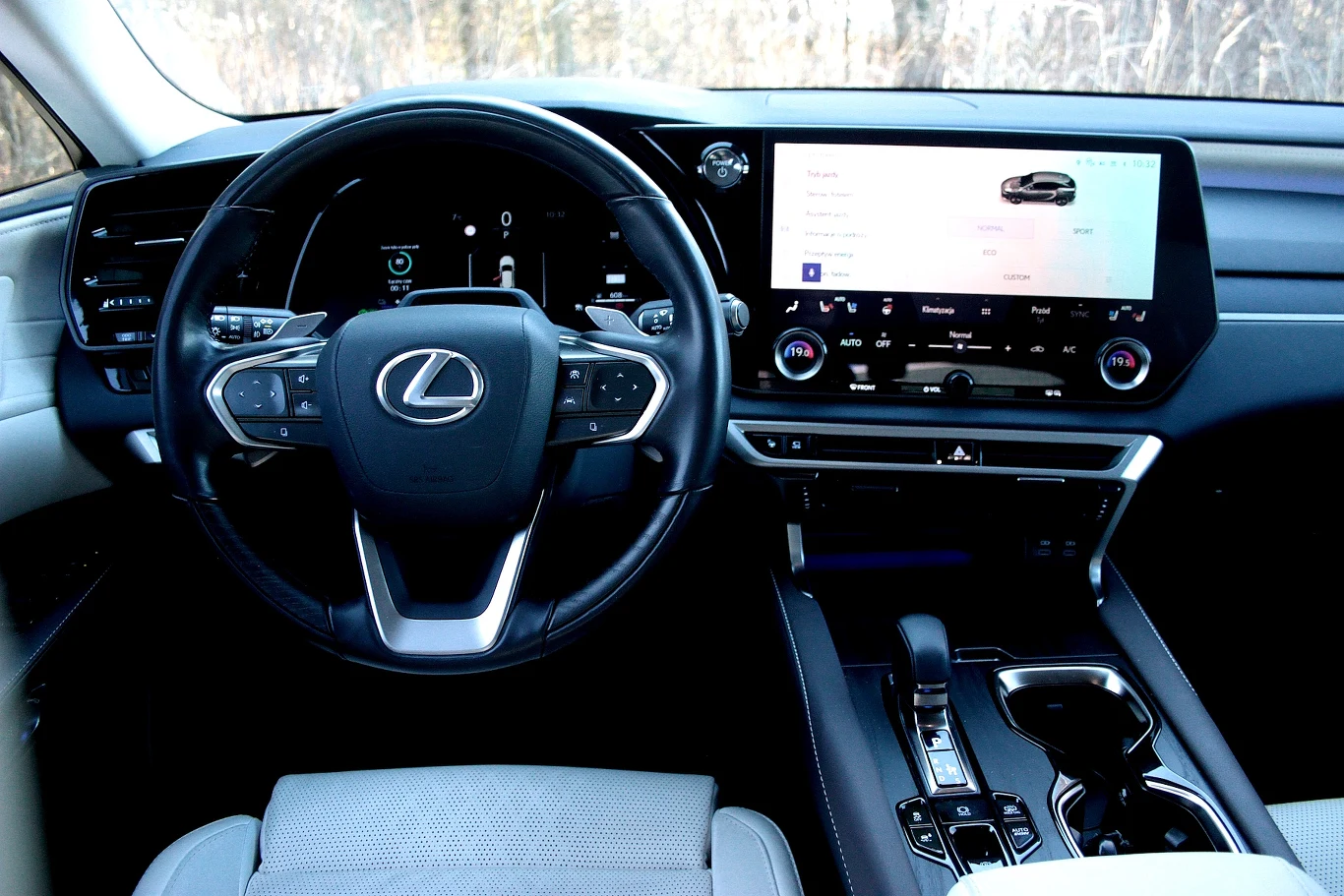 kokpit luksusowego samochodu Lexus z centralnie umieszczonym logo na kierownicy, dużym wyświetlaczem multimedialnym z menu samochodu, nowoczesnymi przyciskami i pokrętłami na konsoli środkowej oraz eleganckim wykończeniem wnętrza