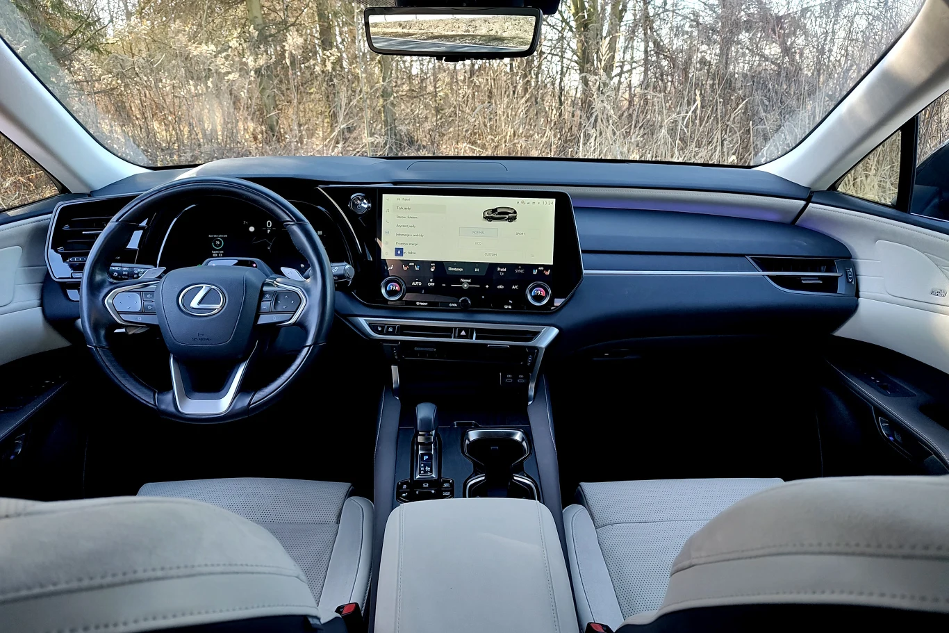 kokpit luksusowego samochodu Lexus z dużym ekranem multimedialnym pośrodku, elegancką kierownicą z logo marki oraz widocznymi skórzanymi fotelami w jasnym kolorze