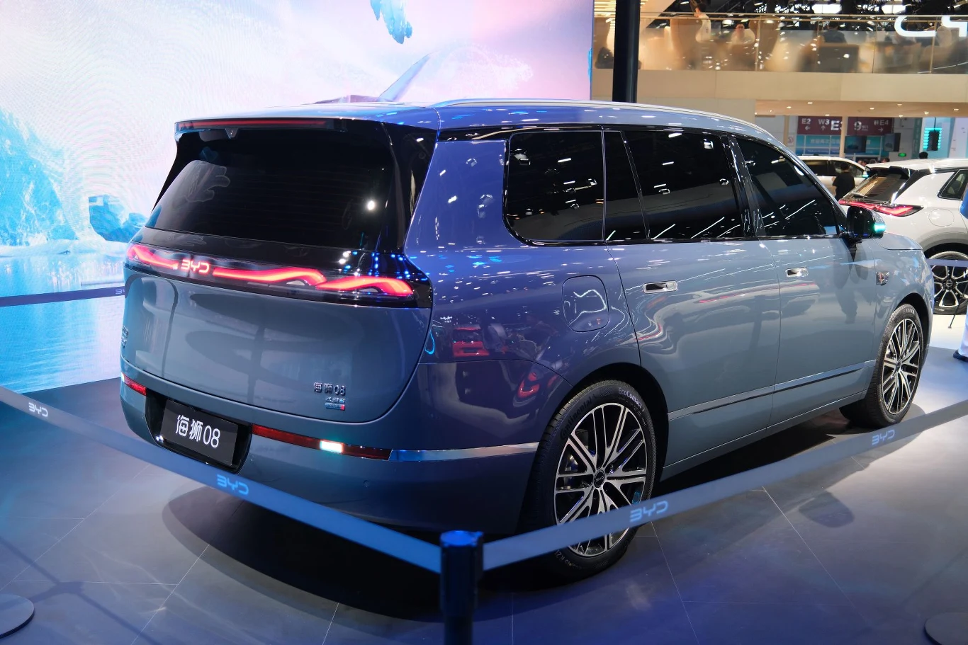 BYD Sealion 08 oraz Seal 08 to kolejno SUV i sedan, które mają pełnić funkcję flagowych modeli w ofercie chińskiej marki. Nowoczesny, niebieski SUV z przyciemnianymi szybami, charakterystycznym pasem świetlnym LED na tylnej klapie oraz dużymi felgami, prezentowany na salonie samochodowym za barierkami ochronnymi.