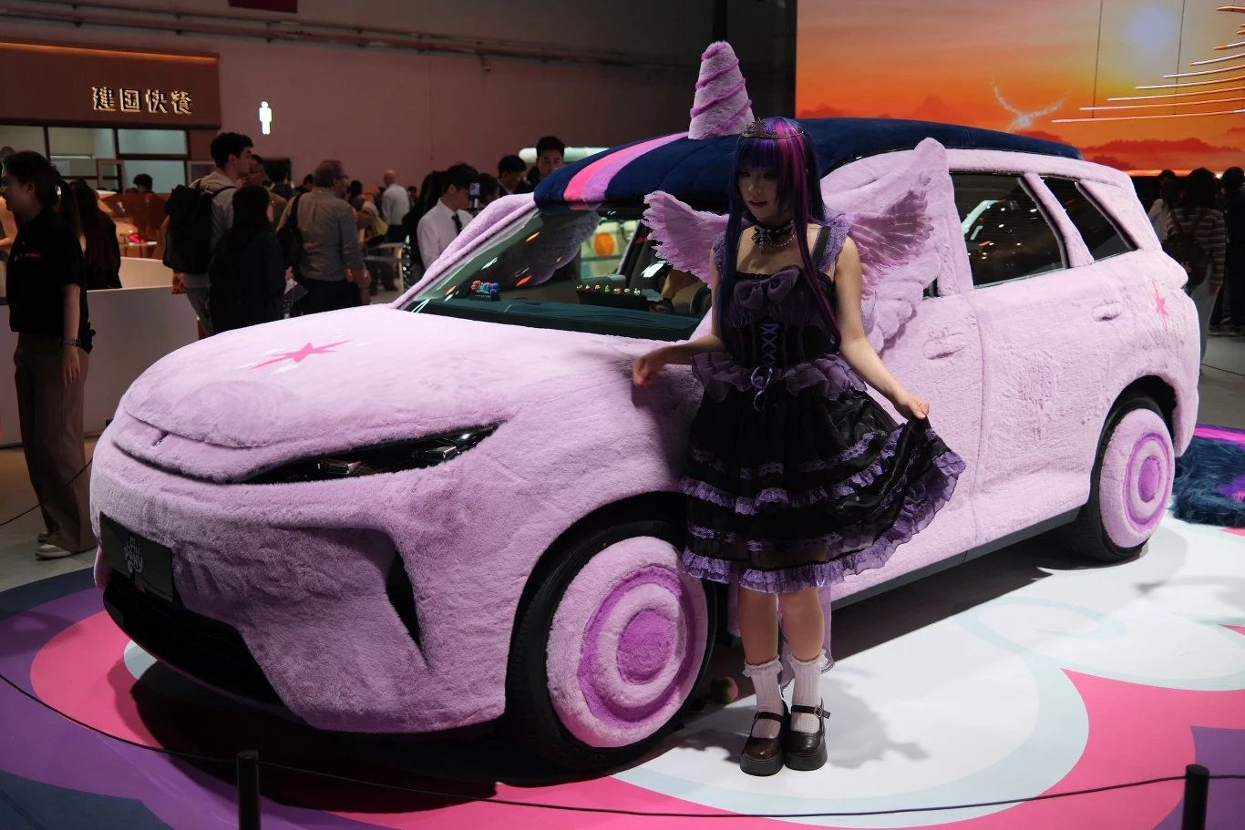 BYD Yuan Plus (w Europie Atto 3) ucharakteryzowany na jednorożca. Jest to efekt współpracy z My Little Pony. samochód pokryty różowym, pluszowym materiałem stylizowany na postać z kreskówki, z wystającym rogiem i uszami na dachu, ozdobiony gwiazdą na masce; obok stoi kobieta w stroju cosplay z peruką, skrzydłami i fioletową sukienką, nawiązująca do tej samej ...