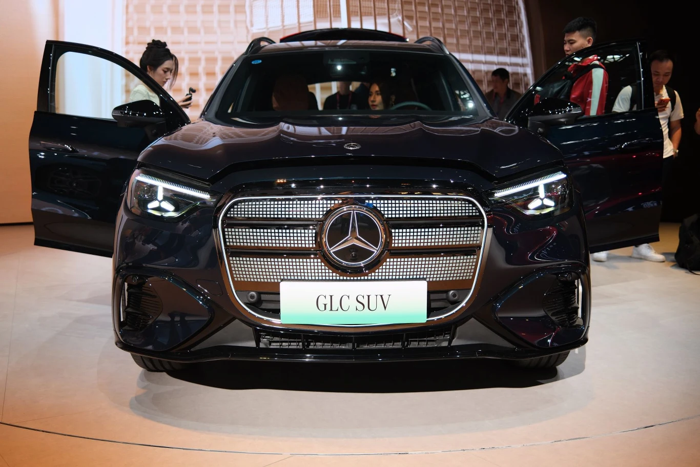 Elektryczny Mercedes GLC ma przejeżdżać do 672 km na jednym ładowaniu. Nowoczesny Mercedes-Benz GLC SUV w czarnym kolorze, z charakterystycznym, chromowanym grillem oraz otwartymi drzwiami po obu stronach; wokół samochodu stoi kilka osób zwracających uwagę na pojazd.