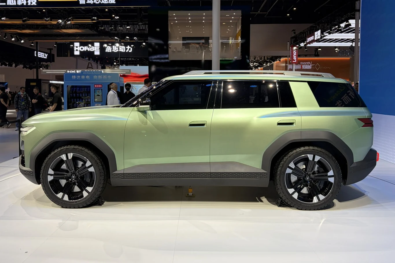 Koncepcyjna Jetta X jest reprezentantem nowego języka stylistycznego "Modern Robust" zielony, nowoczesny SUV o wyrazistych, geometrycznych liniach nadwozia, dużych czarnych felgach i kontrastowych czarnych nadkolach, ustawiony w jasnym, wystawowym otoczeniu z widocznymi elementami ekspozycji motoryzacyjnej w tle