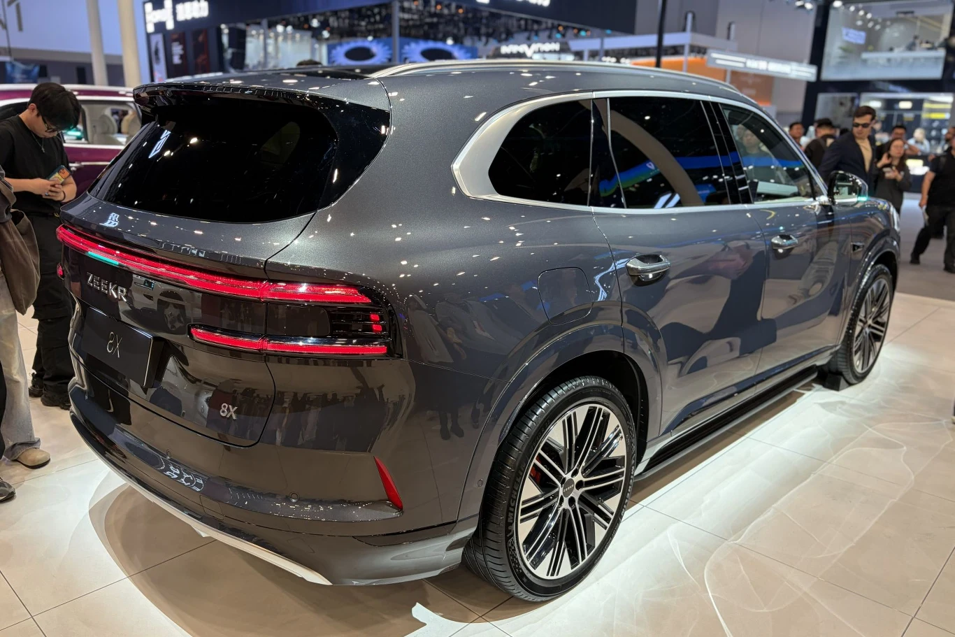 Zeekr 8X to duży SUV, który potrafi rozpędzić się do 100 km/h w 2,96 sekundy. nowoczesny SUV o eleganckiej, ciemnoszarej karoserii, efektowne tylne światła LED biegnące przez całą szerokość pojazdu, masywne alufelgi oraz sportowa linia nadwozia w salonie samochodowym z licznymi odwiedzającymi