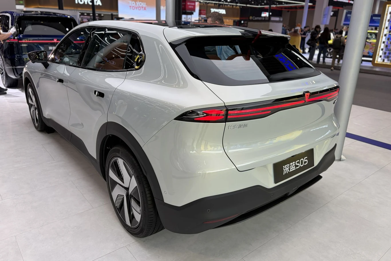 Changan zaczął sprzedaż w Europie od dwóch elektrycznych SUV-ów: Deepal S05 (na zdjęciu) i Deepal S07. biały nowoczesny samochód elektryczny typu SUV z jednolitym, poziomym pasem tylnych świateł LED, masywnym zderzakiem oraz aerodynamicznymi felgami, ustawiony na tle targowej ekspozycji