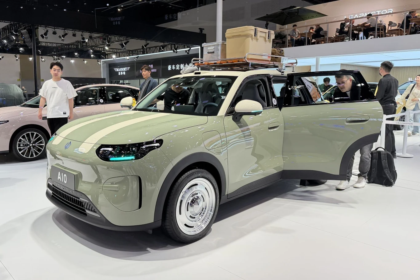 Leapmotor A10 u nas będzie oferowany jako B03X. zielony samochód elektryczny z otwartymi drzwiami, białym dachem i brązowym bagażnikiem dachowym z walizkami, wokół którego stoją zainteresowani zwiedzający na targach motoryzacyjnych