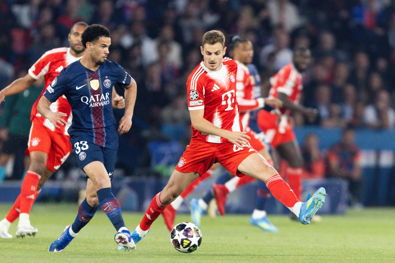 piłkarz w czerwono-białym stroju Bayernu Monachium próbuje odebrać piłkę zawodnikowi w granatowej koszulce Paris Saint-Germain podczas meczu piłkarskiego, wokół nich kilku innych zawodników w ruchu