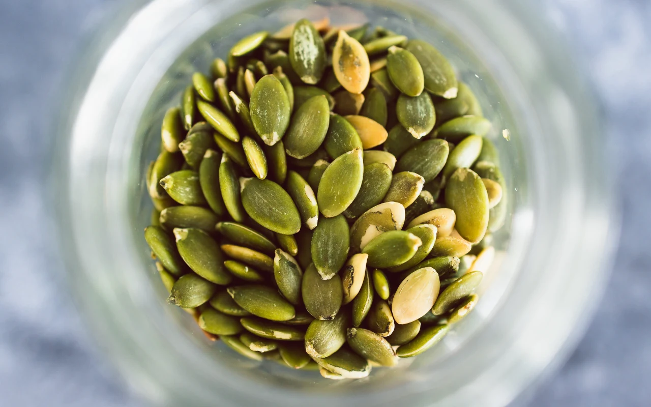 zielone pestki dyni zebrane w szklanym słoiku, wyraźnie widoczne z góry dzięki jasnemu oświetleniu