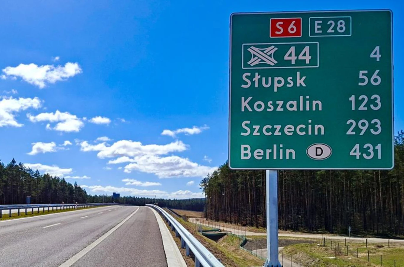 Nowy fragment S6 robi wrażenie. Najdłuższy odcinek już dostępny. Zielona tablica drogowa z kierunkami na Słupsk, Koszalin, Szczecin, Berlin; obok szeroka, pusta S6 w lesie