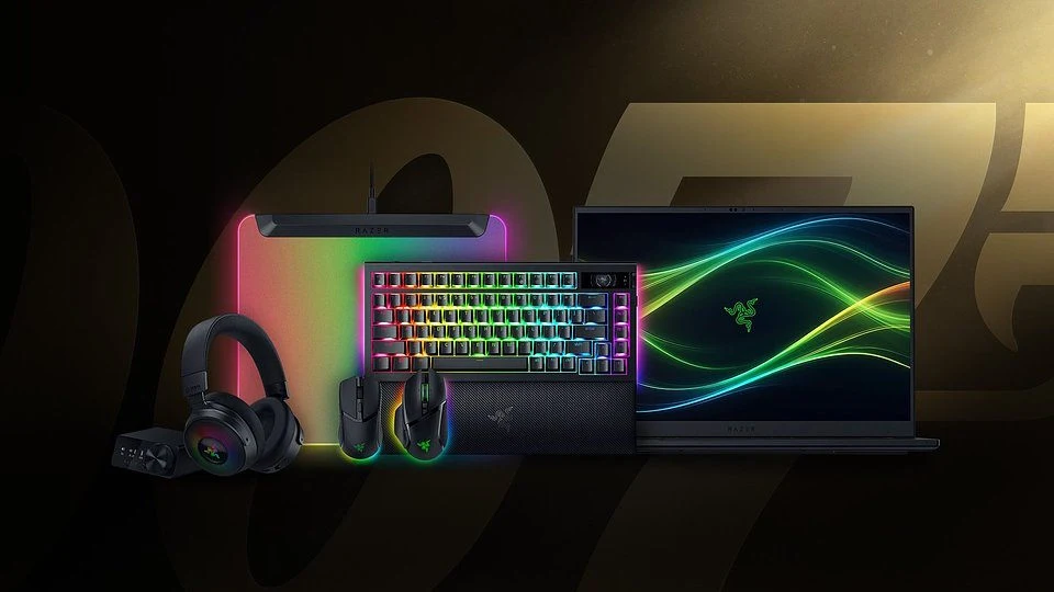 Zestaw urządzeń i akcesoriów gamingowych Razer obejmujący laptop, podświetlaną klawiaturę, myszkę, słuchawki oraz podkładkę, z wyraźnymi efektami świetlnymi RGB i nowoczesnym designem na ciemnym tle.