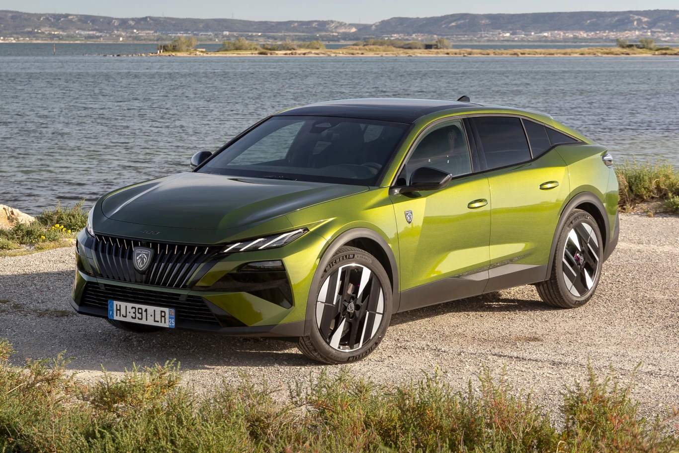 Peugeot 408 po liftingu. Co dostaniemy za 150 tys. zł? Zielony Peugeot 408 po liftingu na żwirze nad wodą, w tle góry.