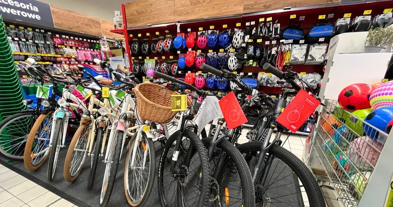 Rowery wracają do łask. Carrefour przecenił te modele przed majówką Rząd rowerów przed regałem z kaskami i akcesoriami rowerowymi w sklepie Carrefour, obok kosze z piłkami.