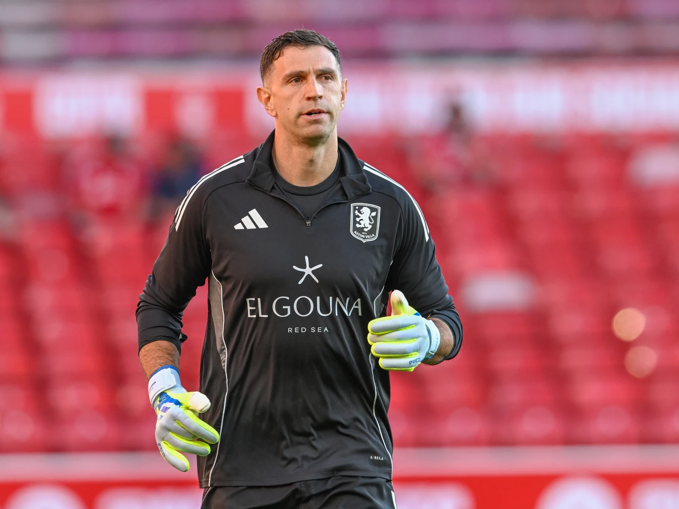 bramkarz w czarnym stroju sportowym z logo El Gouna, ubranego w rękawice bramkarskie, stoi na stadionie z czerwonymi trybunami w tle