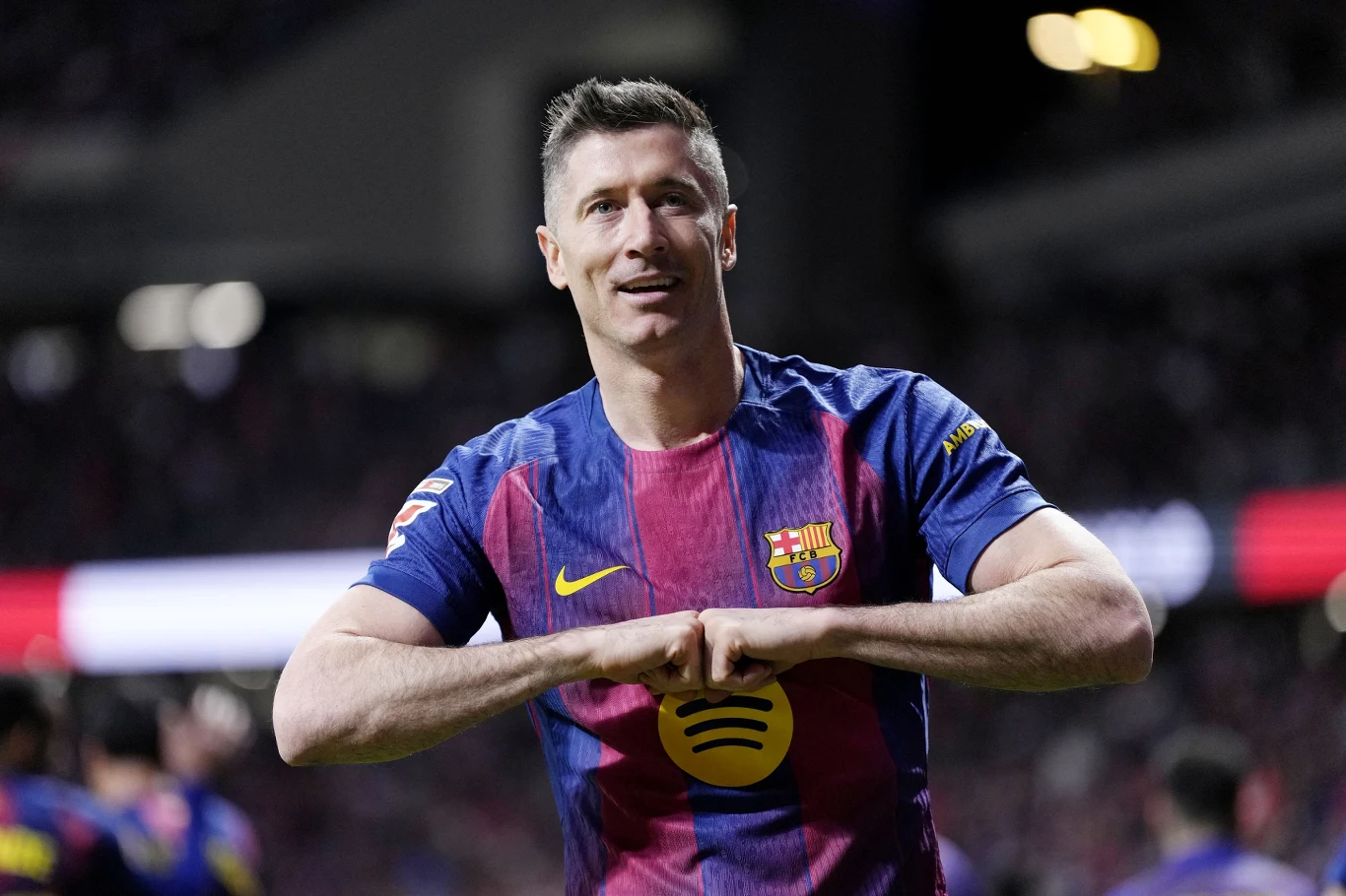 piłkarz FC Barcelony w granatowo-bordowej koszulce wykonuje gest serca rękoma na tle rozmytego stadionu z kibicami w tle