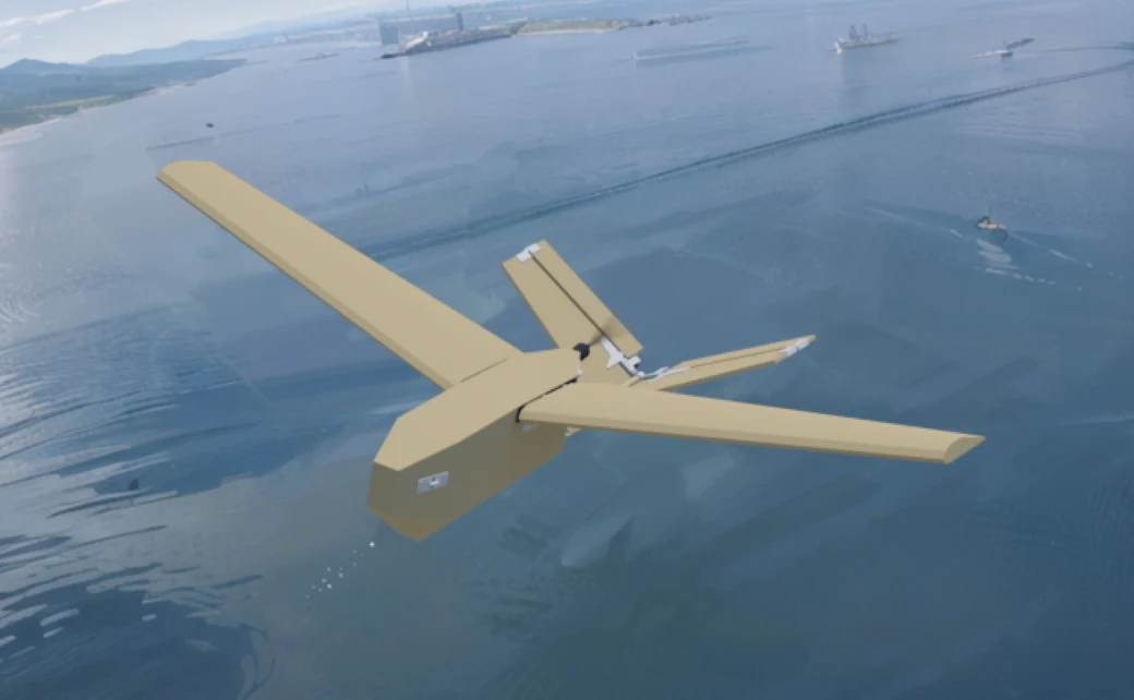 Minister obrony Japonii zaprezentował tekturowe drony-cele firmy Air Kamuy. Zdj. poglądowe. Tekturowy wojskowy dron-cel firmy Air Kamuy o piaskowym kolorze leci nad wodą, w tle statki i brzeg.