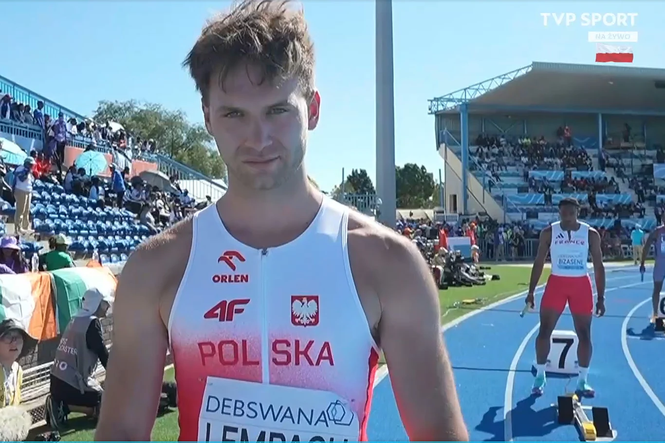 Jakub Lempach, Gaborona 2026 lekkoatleta w stroju reprezentacji Polski stoi na bieżni stadionu lekkoatletycznego, w tle widoczni pozostali zawodnicy, trybuny z kibicami oraz fragment stadionowej infrastruktury
